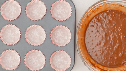 Chocolate muffins or chocolate cupcakes recipe. Chocolate batter in a bowl, and muffin pan with cupcake liners, close up view from above
