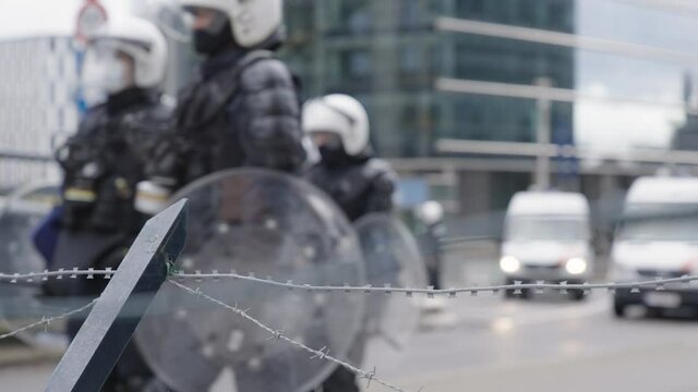 Unrecognizable riot police in full riot gear backed by anti-riot vans cordon off a street during a demonstration - Focus on barbed wire fence