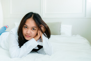 Portrait Cute Asian teen with long hair Wearing a white shirt and lazing around in bed happily in the bedroom.