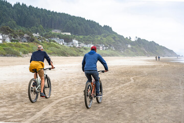 Naklejka premium An elderly father and a young son travel side by side on bicycles along the Pacific Ocean preferring an active healthy lifestyle tempering the body in any weather