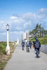 Group of amateur cyclists rides bicycles along the footpath along the Pacific coast preferring an active healthy lifestyle