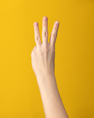 Female hand gesture on yellow background. Woman hand isolated showing index, middle and ring three fingers.