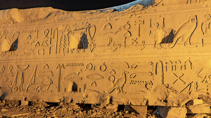 A fragment of an ancient wall in the Egyptian temple of Kom Ombo. Hieroglyphs and drawings carved on the stone are visible. Night illumination.