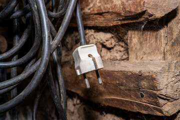 Black extension cord with a white plug hangs in an old shed made of mud and wood
