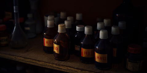 Old dusty bottles with chemicals on a shelf in the science classroom. Substances for experiments in dark glass bottles with inscriptions, close-up. Concept of school education.