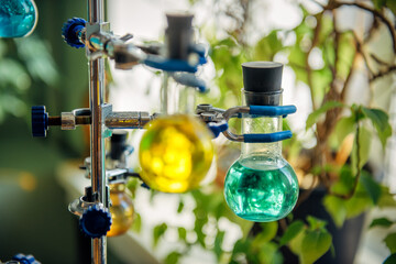 Scientific glass flasks containing green and yellow chemical reagent liquid holding by clamp for...