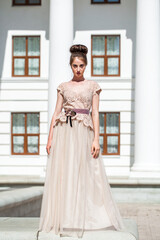 Obraz premium Young woman in a luxurious beige dress posing on the street