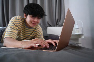 Smiling young man freelancer working with laptop computer on bed.