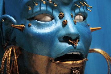 Face sculpture, fantastic creature. Female face, painted in blue and gold. Golden metallic decorations and ornaments. 