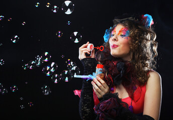 Fashionable young model female with creative make-up blowing soap bubbles. Doll style. Bright...