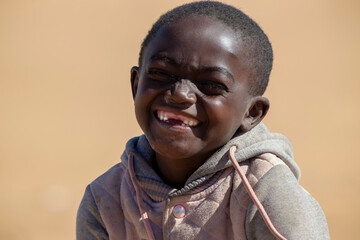 Little african black child stands against the yellow sand on a sunny day