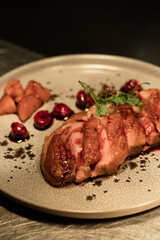 tender meat with fruits, cherries and herbs on a gray ceramic plate in a restaurant in the evening