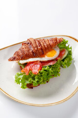 Sandwich from croissant with salted salmon, cucumber, fried egg and lettuce