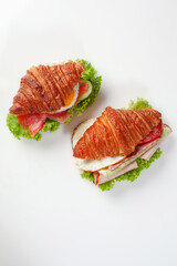 Two croissant sandwiches with fried eggs, salted salmon, ham, fresh cucumbers, tomatoes and lettuce