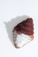 Chocolate croissant sprinkled with powdered sugar and cocoa on white surface