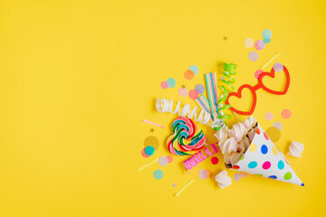 Holiday decor with multicolored confetti near party hat on yellow background