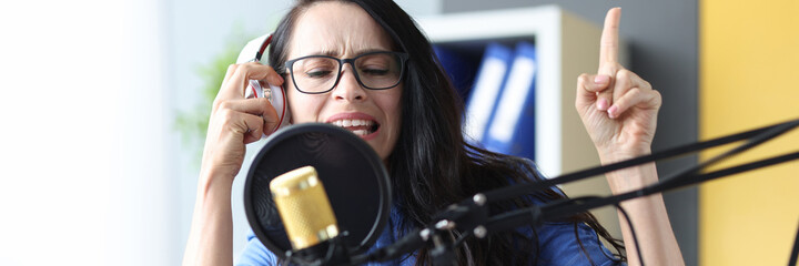Emotional woman radio presenter in headphones speaks into microphone closeup