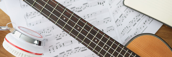 Wooden guitar headphones and music notes on table closeup