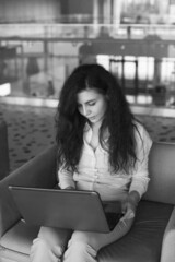 Young woman working on laptop in the public pplace. Caucasian woman with brown hair in the office and using laptop in black and white