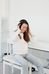 Young woman in white sweatshirt listening to music on headphones at home and smiling