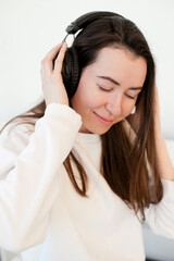 Naklejka premium Young woman in white sweatshirt listening to music on headphones isolated