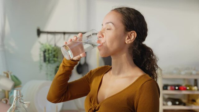Young beautiful Latino woman holding clean water into glass in kitchen. 