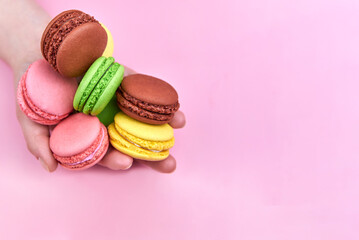 Heap of bright cookies in the hand of a woman on a pink background, copy space.