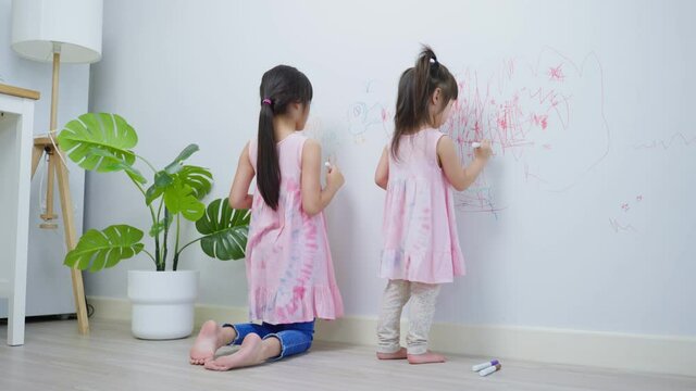 Asian young sibling kid girl enjoy paint on white wall in living room.