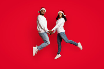 Beautiful black couple in Santa hats holding hands and jumping