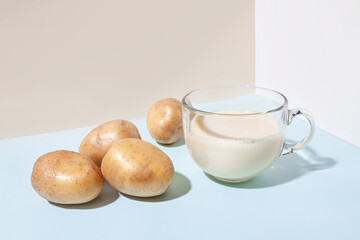 Potato milk. A cup with milk and potato tubers side view. Alternative plant milk