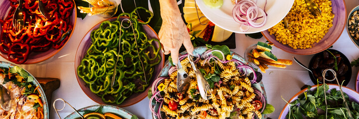 Above vertical banner header view of table full of food from catering service and people ready to...