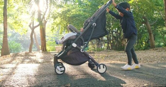 Little boy push baby stroller recreation in tree park sunrise morning