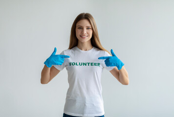 Young caucasian lady showing volunteer t-shirt and smiling at camera, proud and happy of working at charity center