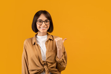 Check this offer. Positive young woman pointing thumb finger aside at free space, advertising your text or design