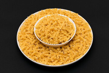Uncooked Fusilli Pasta Lying on White Plate on Black Background. Raw and Dry Macaroni. Unhealthy and Fat Food