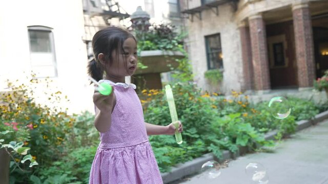 Oriental girl making bubbles, one isolated kid playing alone in the exterior yard