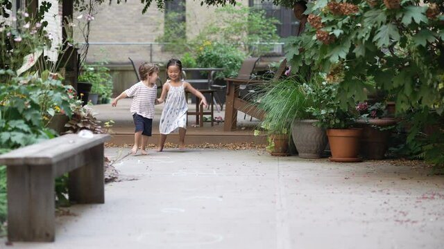 Two super cute kids run toward the camera in slow motion while laughing and having a great time.  Multiracial friendship