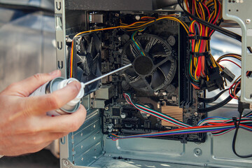 Maintenance and cleaning of the insides of the computer. Man's hand holds a cylinder of compressed air and cleans the insides of the computer - obrazy, fototapety, plakaty