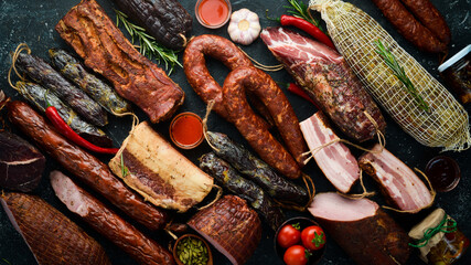 Meat banner. Set of smoked meat, sausages, salami and dried salted meat. On a black stone background.