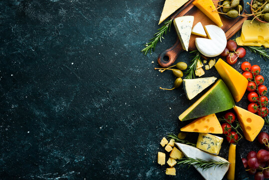 Cheese. Assortment of cheese and snacks on black stone background. Top view. Free space for your text.