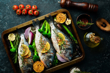 Raw Dorado fish with vegetables in a metal tray. Fish cooking recipe. Top view. Free copy space. On a black stone background.