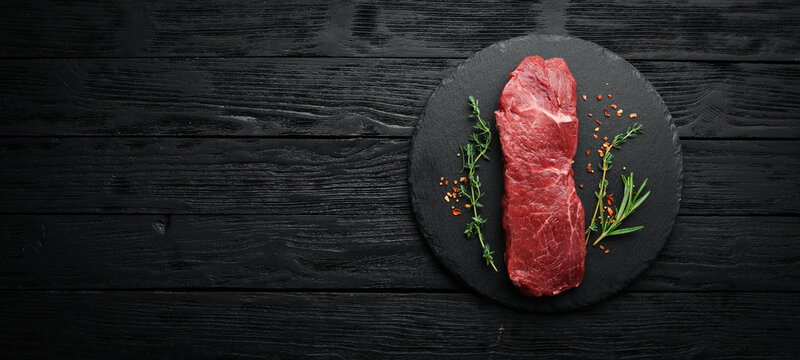 Raw sirloin steak with thyme, rosemary and spices. Top view. Flat lay top view on black stone cutting table.