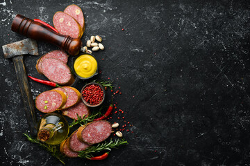 Sliced salami slices with rosemary and spices on a black stone background. Top view. Rustic style.