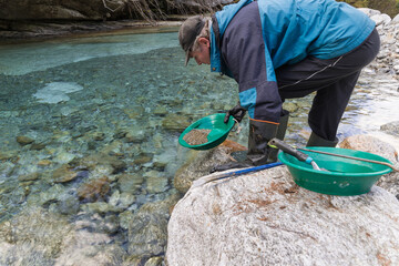 Outdoor adventures on river. Gold panning, search for gold. Man is looking for gold with a gold pan in a mountain stream     