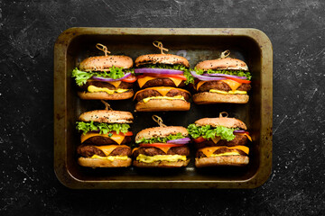 Delicious grilled homemade burgers with beef, tomatoes, cheese, onions and salad. Burger menu. Top view. On a black stone background.
