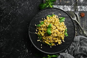 Farfalle pasta with pesto sauce and basil in a black stone plate. Top view. Free space for your text.
