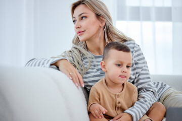 Fototapeta na wymiar Carefree female parent has rest with preschooler son in living room on sofa at home, look at side. Pretty beautiful caucasian family mother and kid activity for indoor weekend or quarantine relax