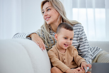 Carefree female parent have rest with preschooler son in living room wathcing cartoons, at home. Cheerful funny family mother and kid activity for indoor weekend or quarantine relax