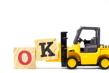 Toy forklift hold letter block k to complete word ok on wood background