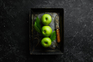 Fruits. Fresh juicy green apples on a tray. Rustic style. On a black stone background.